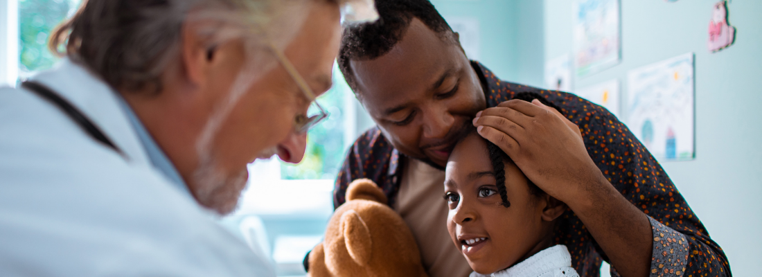 Male doctor examines child patient while her father sits with her Male doctor examines child patient while her father sits with her