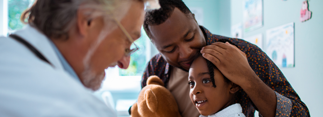 Male doctor examines child patient while her father sits with her