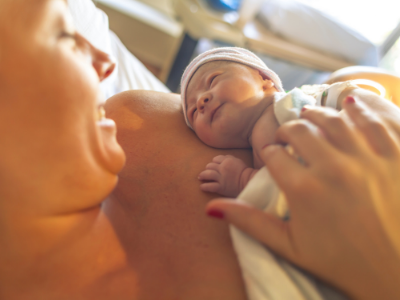 Smiling mother looking down at her newborn baby while laying in a hospital bed