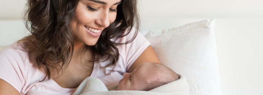 A mother smiles as she looks at her newborn baby, held in her arms