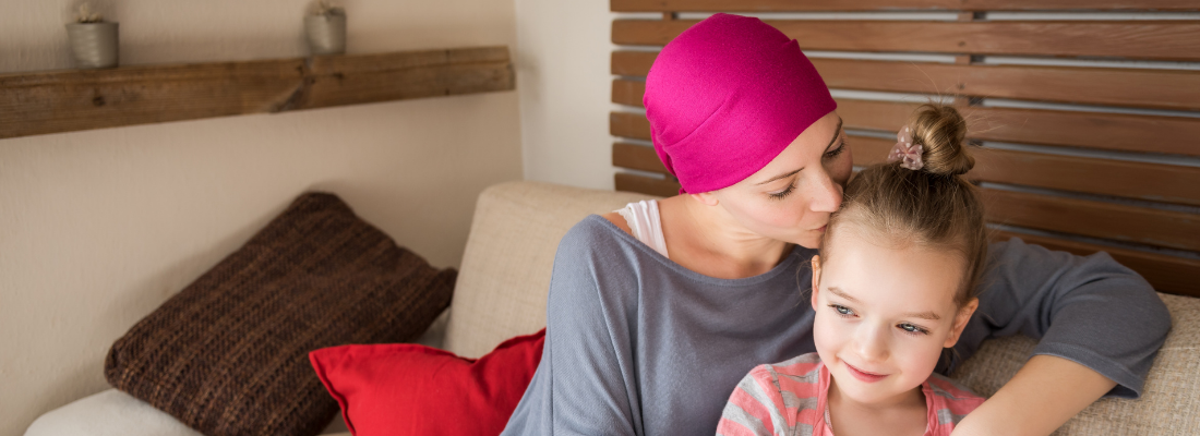 Young female cancer patient kissing her young daughter on her head.
