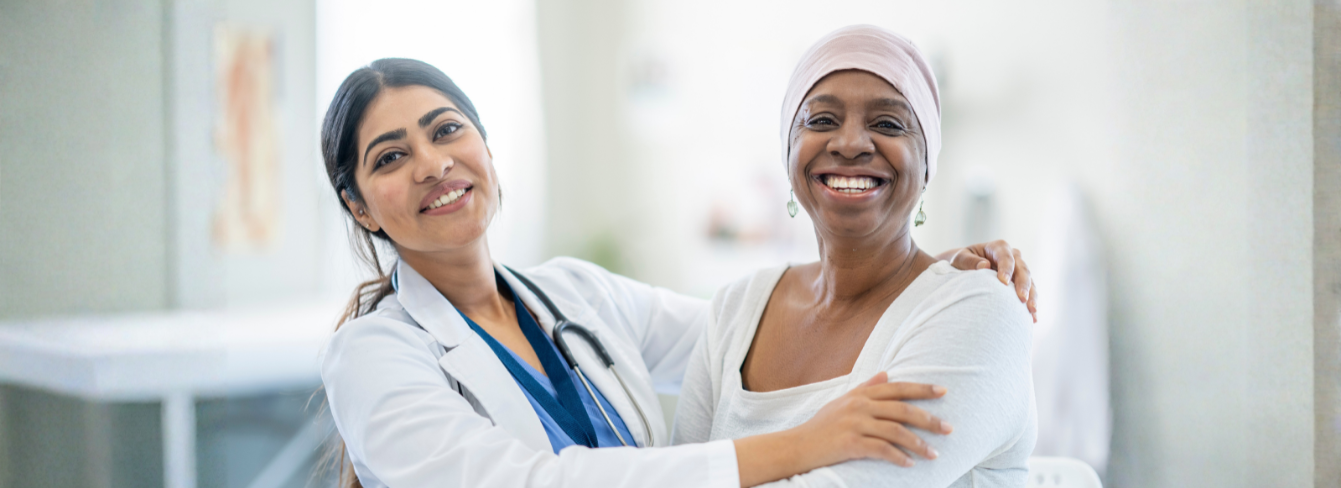 A smiling female physician with a smiling female cancer patient in a medical office