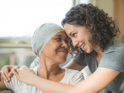 Female cancer patient smiles as her adult daughter hugs her