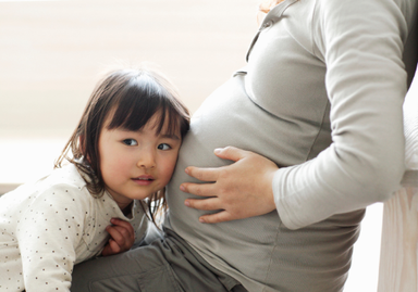 A little girl presses her ear to her mother's pregnant belly