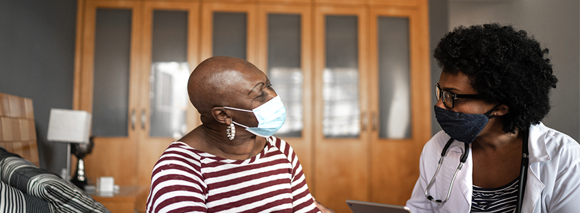 A female physician talks with a female patient, both wearing masks. A female physician talks with a female patient, both wearing masks.