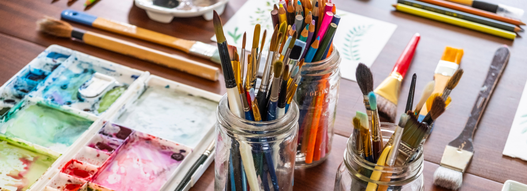 Paints, brushes in jars, and other art supplies on a table.