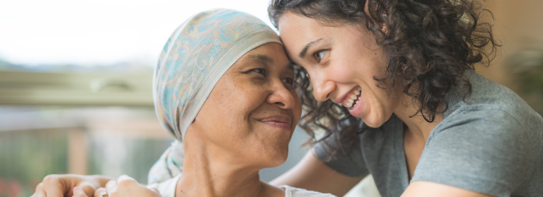 Female cancer patient in wearing headwrap being hugged by adult daughter