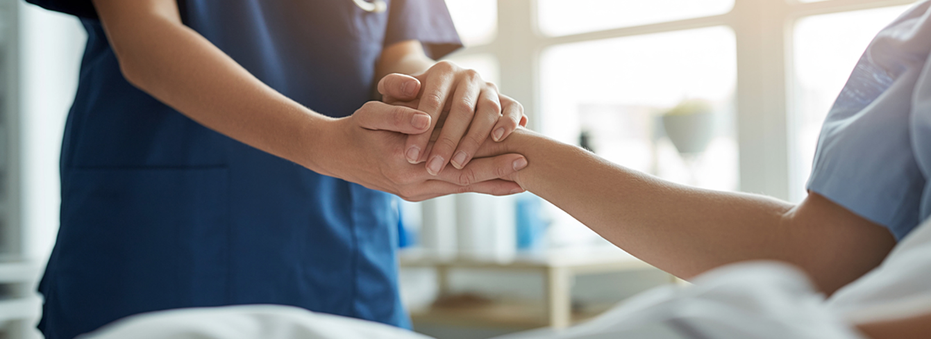 Hospital caregiver holding the hand of a patient in a hospital bed