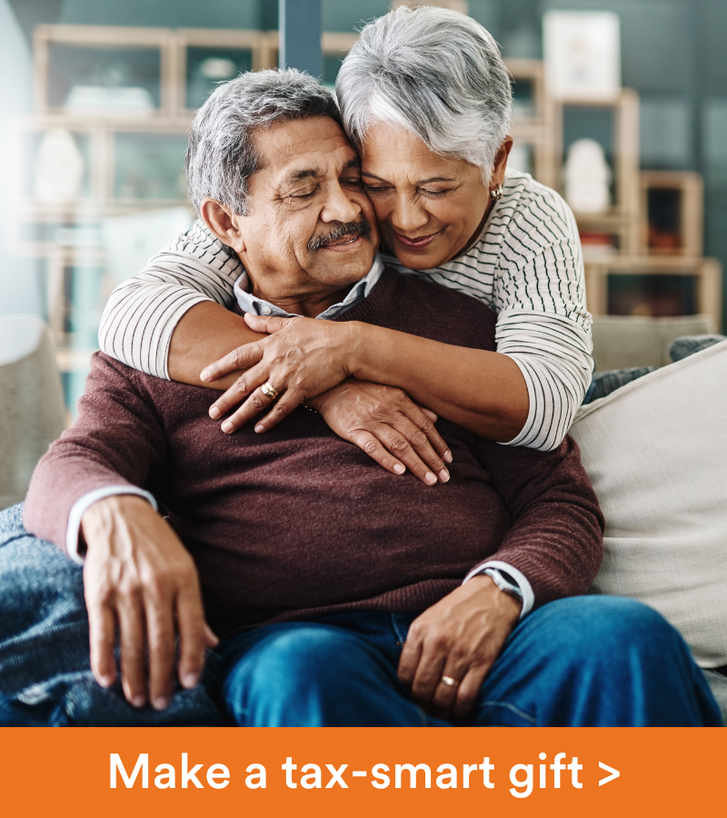 A older woman stands behind her husband, with her arms around him. Copy reads "Make a tax-smart gift"