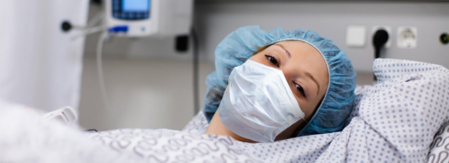 Portrait of a female hospital patient in a hospital bed, wearing a mask