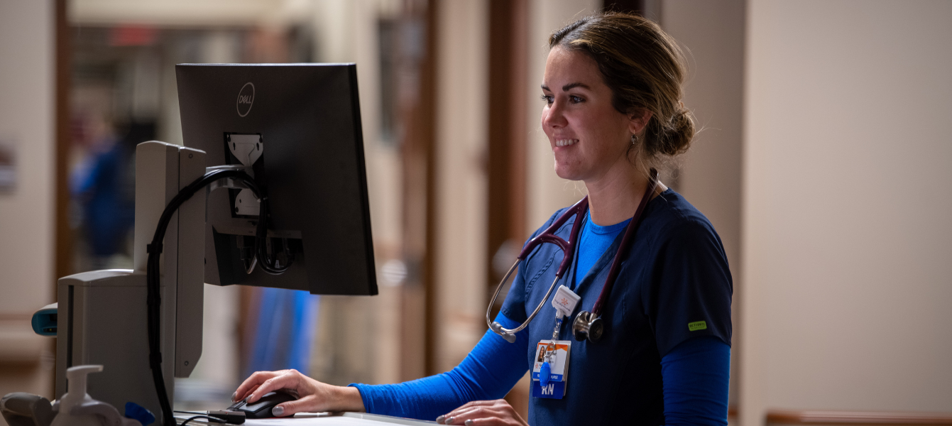 Young, female French Smiling female nurse working at computer. nurse in mask standing in a patient room