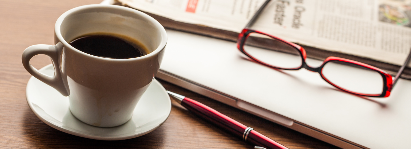 A newspaper and glasses sit on a closed laptop next to a cup of coffee A newspaper and glasses sit on a closed laptop next to a cup of coffee