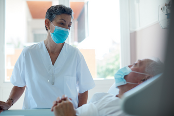 Female nurse in a mask comforts a hospital patient