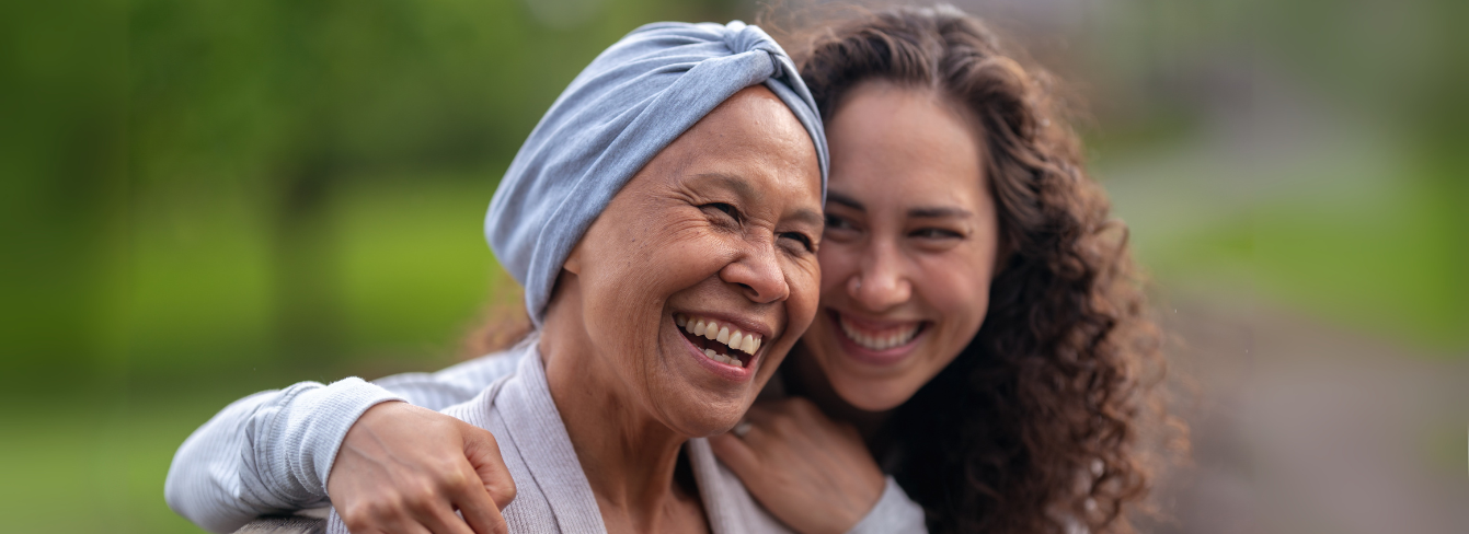 A cancer patient in a headwrap laughs with her adult daughter A cancer patient in a headwrap laughs with her adult daughter