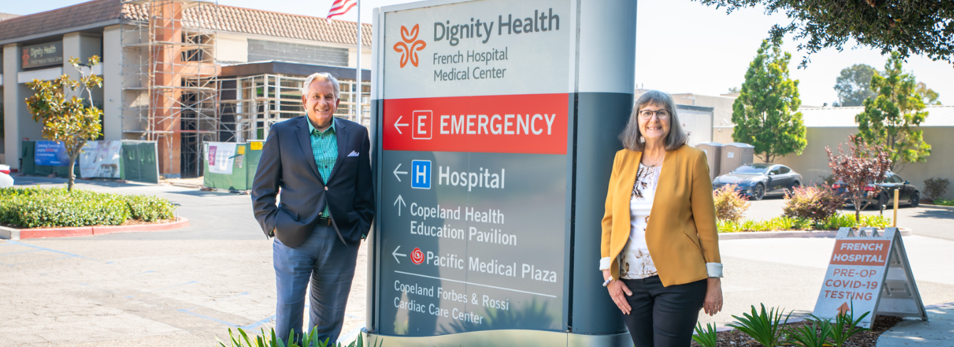 Alan Iftiniuk and Debby Nicklas stand next to the French Hospital entrance sign, with the hospital in the background.