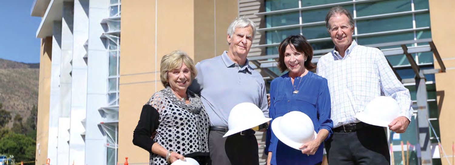 Four adults outside hospital construction holding hard hats Four adults outside hospital construction holding hard hats