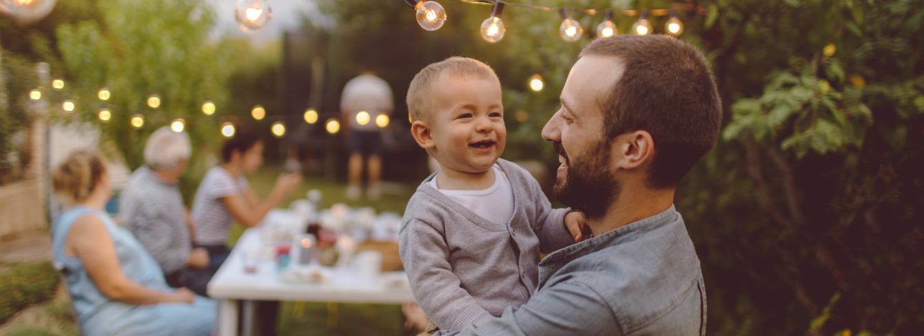 Family garden party with a father holding his toddler in the foreground