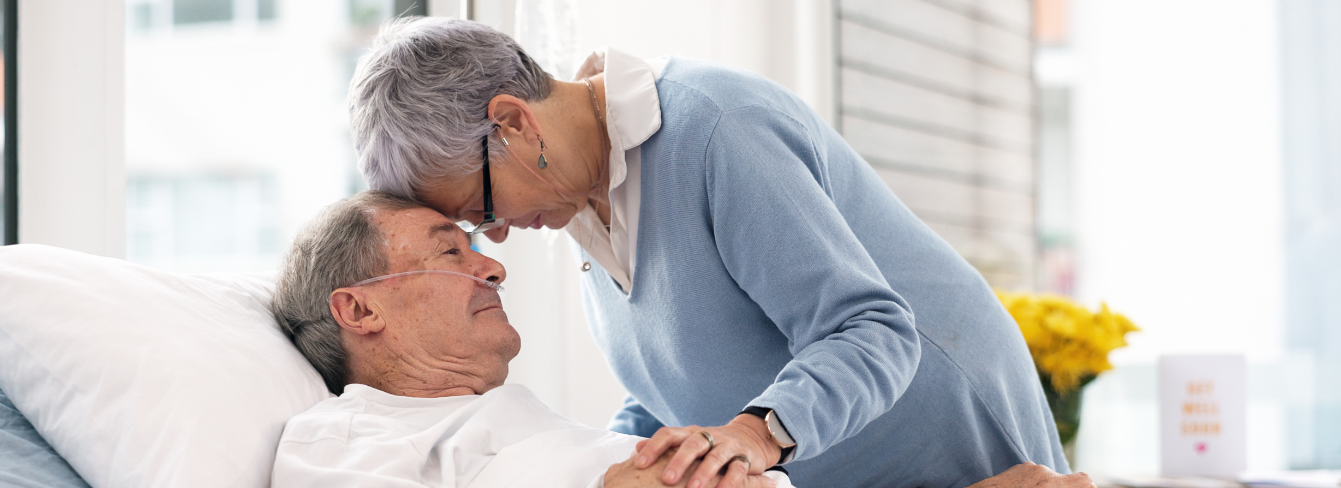 An elderly male patient in a hospital bed is comforted by his wife   