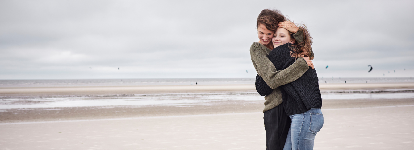 A mother hugs her teenage daughter at the beach